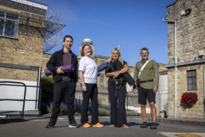 2 men and 2 women holding yoga mats outside a prison